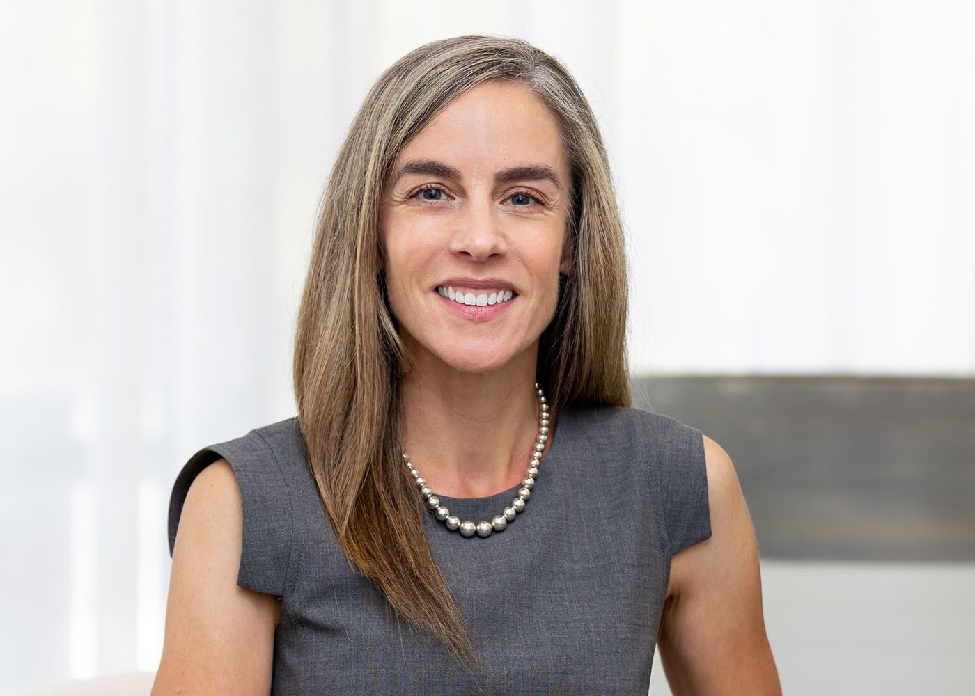 Smiling woman in professional attire with pearls.