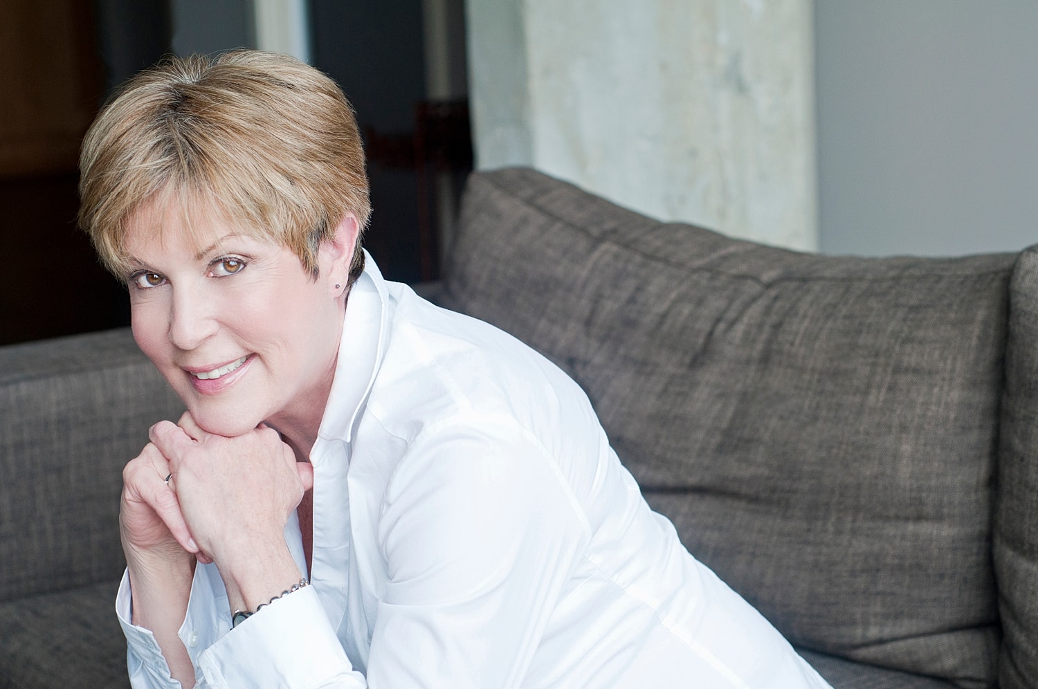 Smiling woman in white shirt, seated on couch.