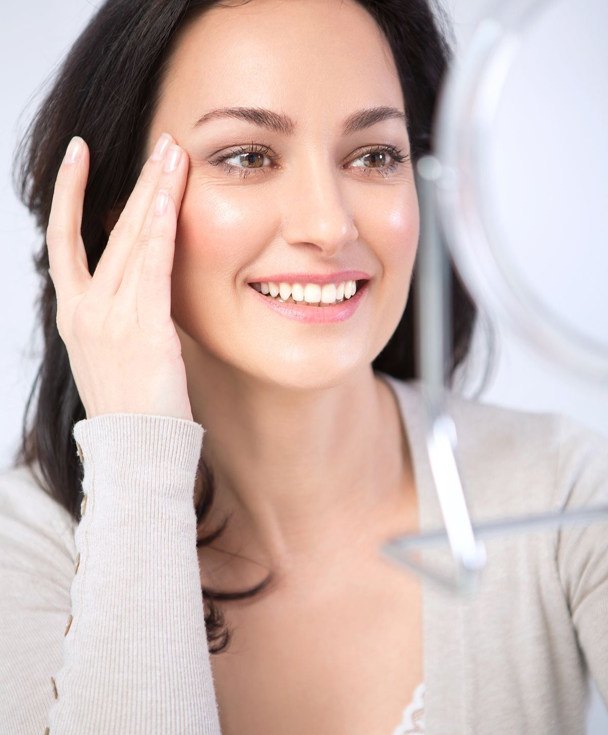 Smiling woman looking in mirror, applying skincare.