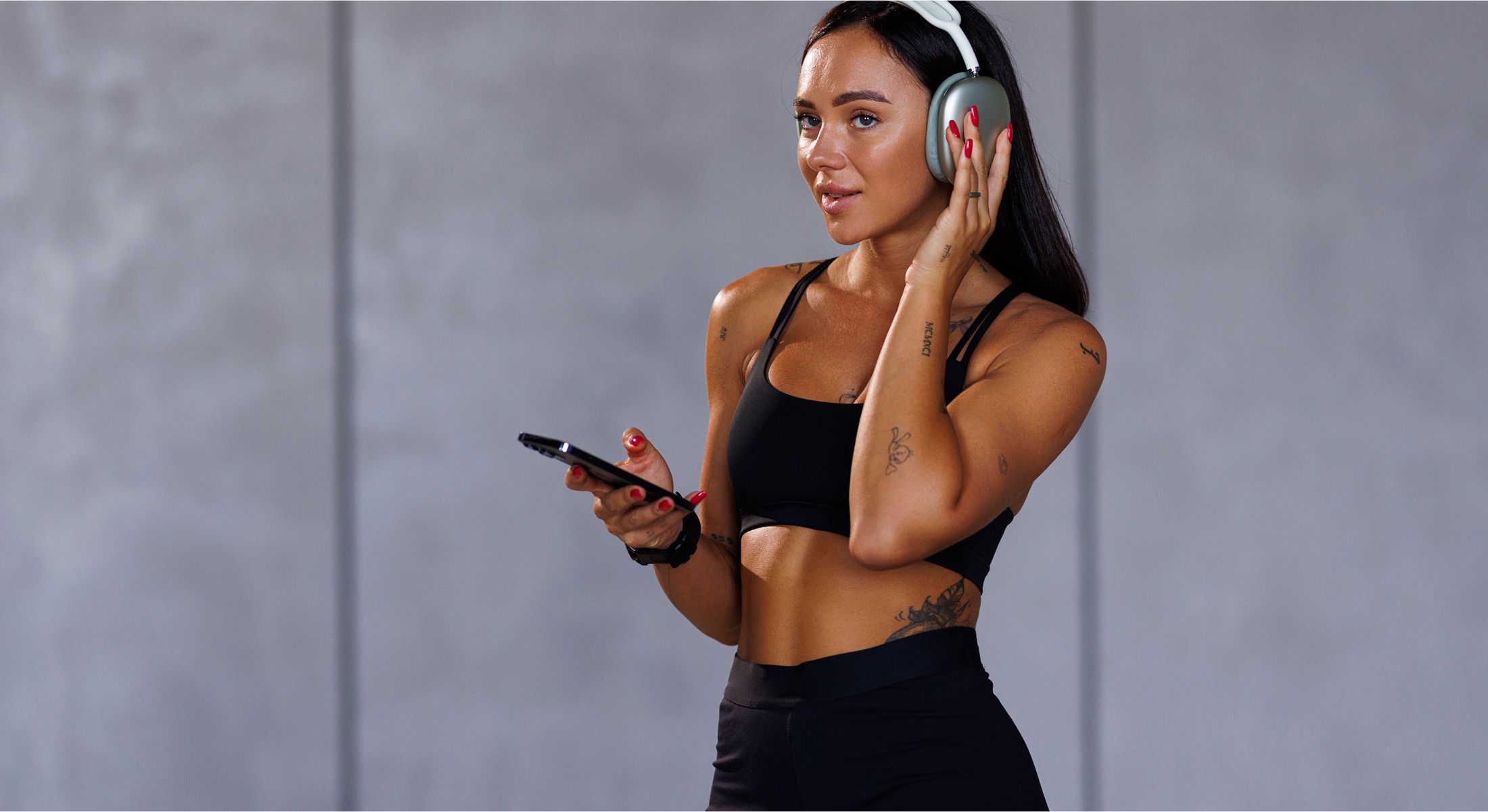Woman wearing headphones while holding smartphone.
