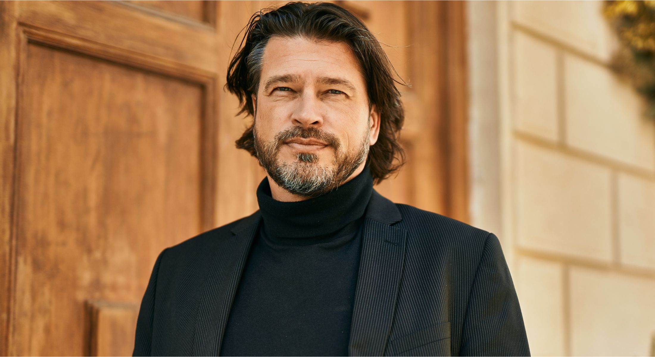 Man in a black turtleneck and blazer outdoors.