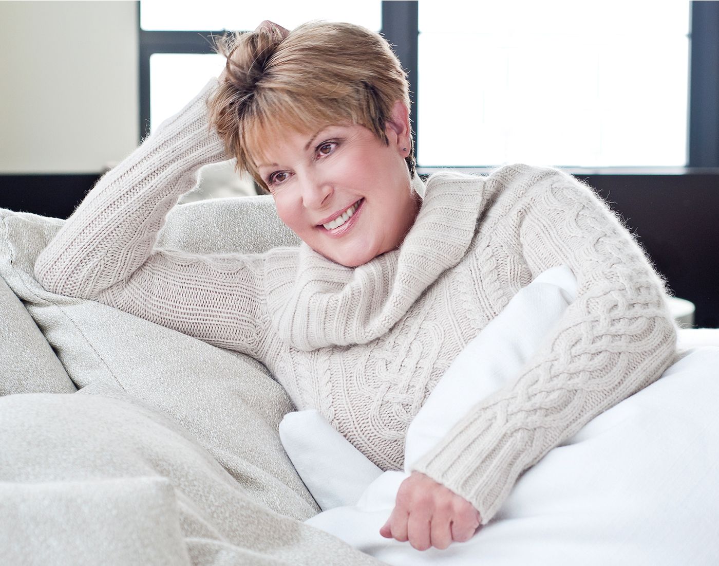 Smiling woman in cozy sweater on couch.