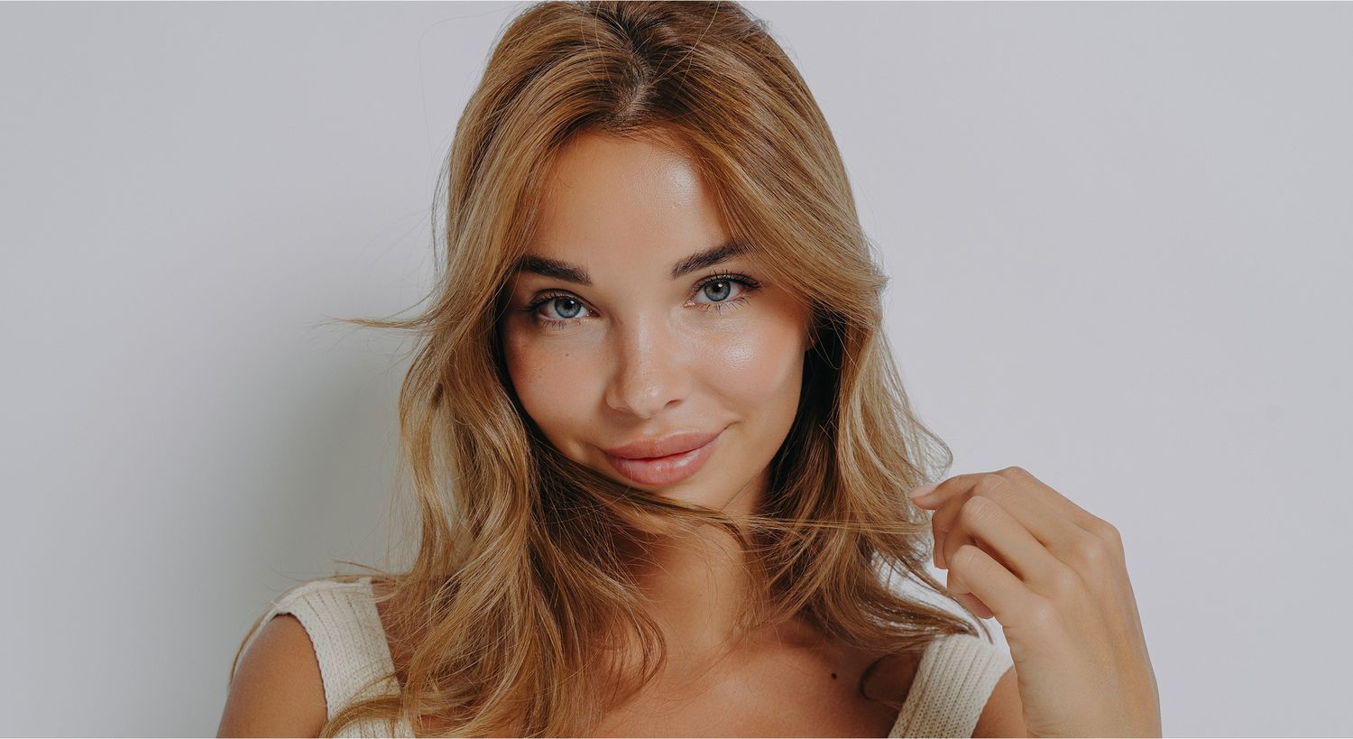 Smiling woman with wavy hair on neutral background.