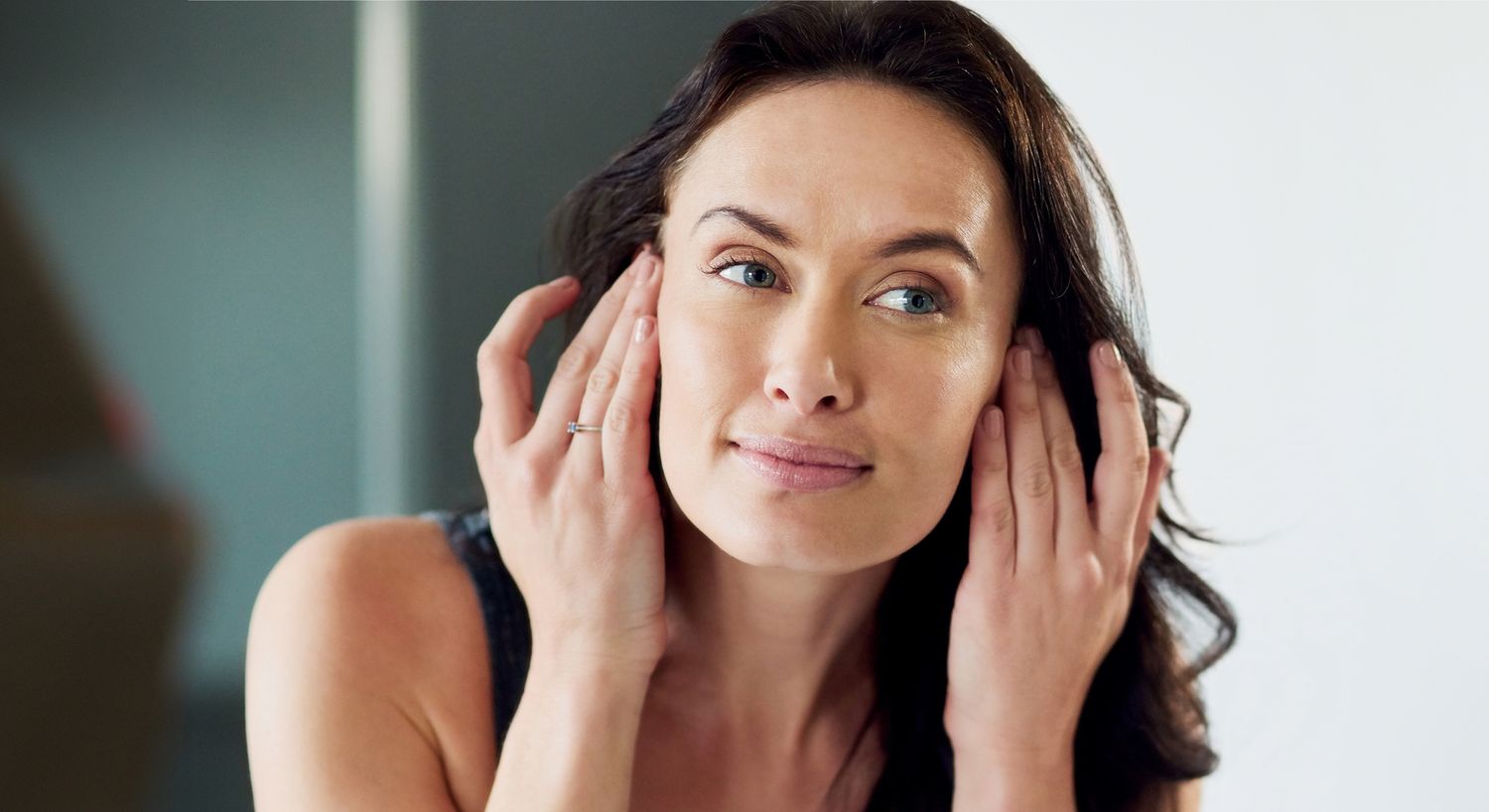 Woman applying skincare in front of mirror.